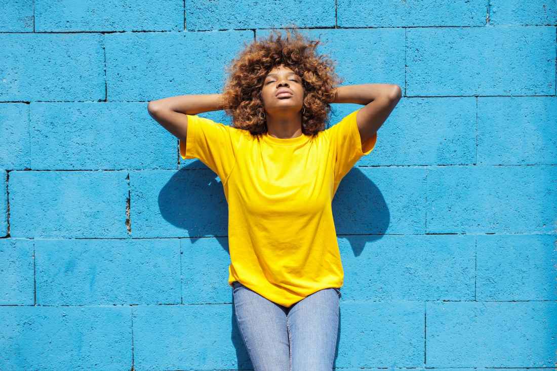 a lady in yellow shirt leaning against blue brick wall